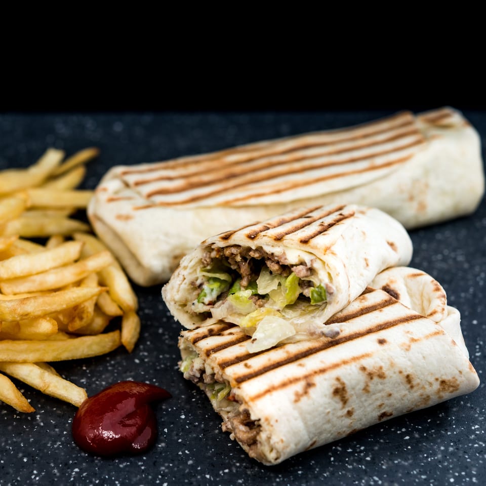 Two grilled burritos, one cut open to show meat and lettuce, served with fries and ketchup.