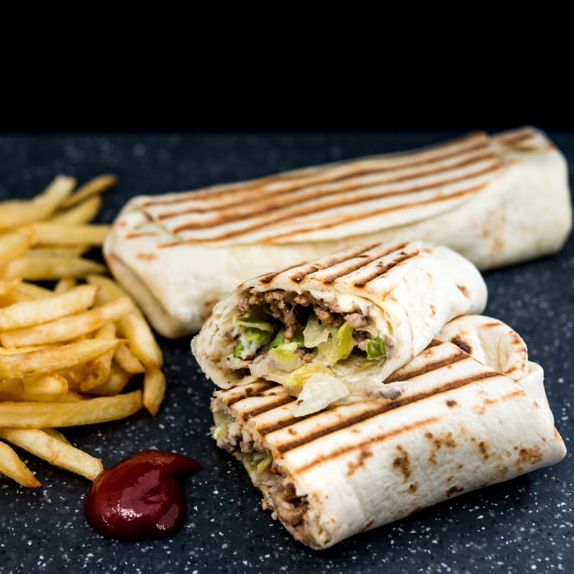 Two grilled burritos, one cut open to show meat and lettuce, served with fries and ketchup.