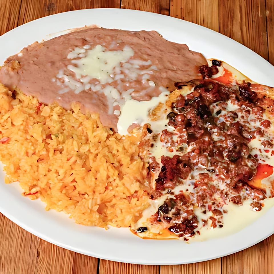 A white plate holds Mexican rice, refried beans with cheese, and a meat dish with white sauce.