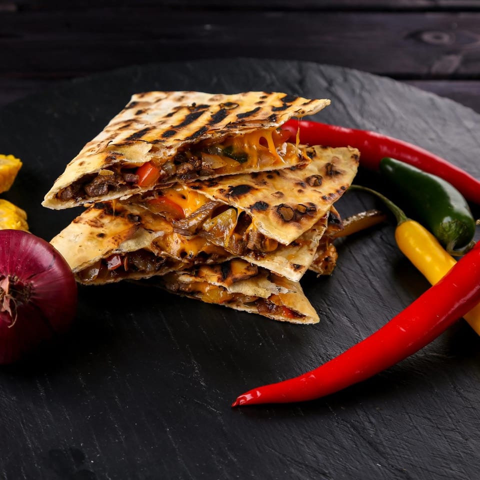 Stack of cheesy Tequila Mexican Restaurant quesadillas with red onion and colorful chili peppers.