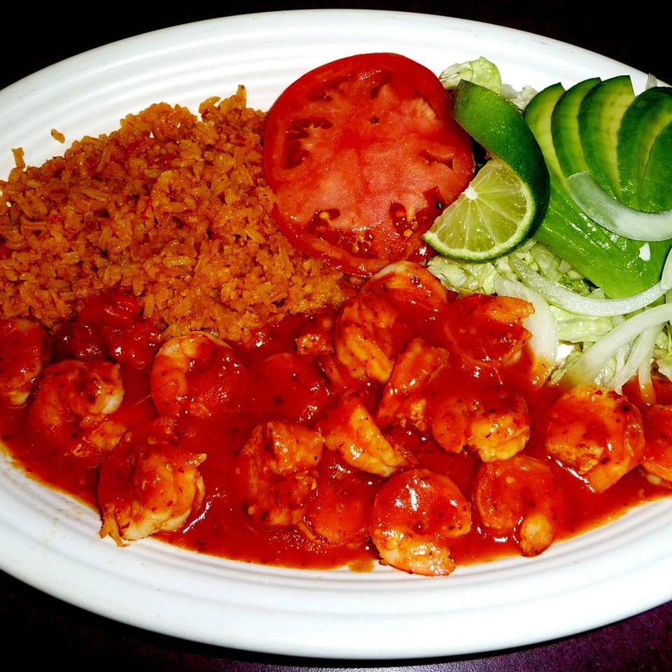 Shrimp in red sauce with Mexican rice, sliced tomato, avocado, lime, and lettuce.