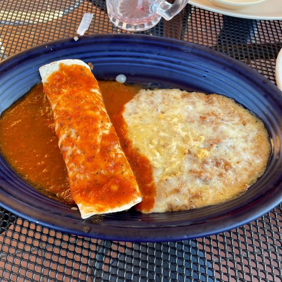 A Tequila Mexican Restaurant burrito covered in red sauce and melted cheese, next to a side of refried beans.