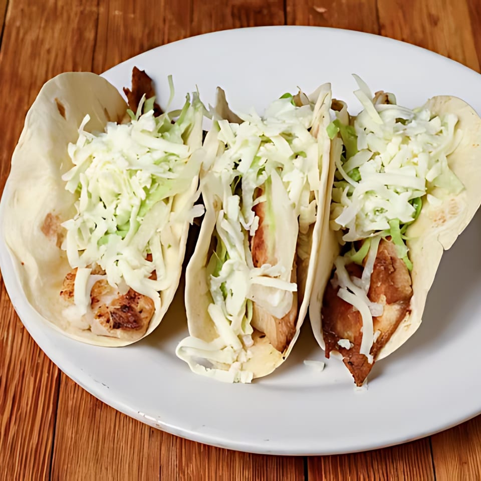 Three Tequila Mexican Restaurant tacos with meat, shredded cabbage, and cheese on a white plate.